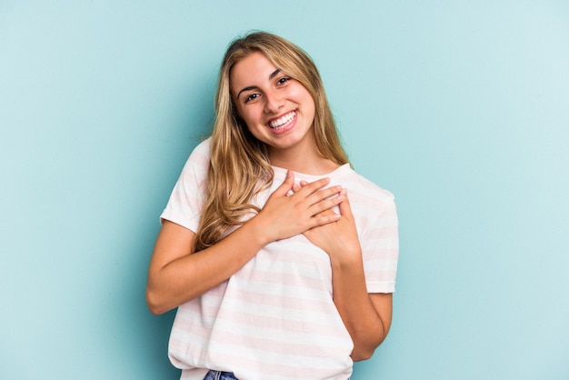 Jonge blanke blonde vrouw geïsoleerd op blauwe achtergrond heeft vriendelijke uitdrukking, palm op borst drukken. Liefdesconcept.