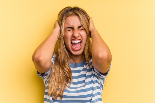 Foto jonge blanke blonde vrouw geïsoleerd op gele achtergrond die oren bedekt met handen die proberen niet te hard geluid te horen.