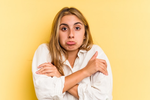 Jonge blanke blonde vrouw geïsoleerd op gele achtergrond haalt schouders op en open ogen verward.