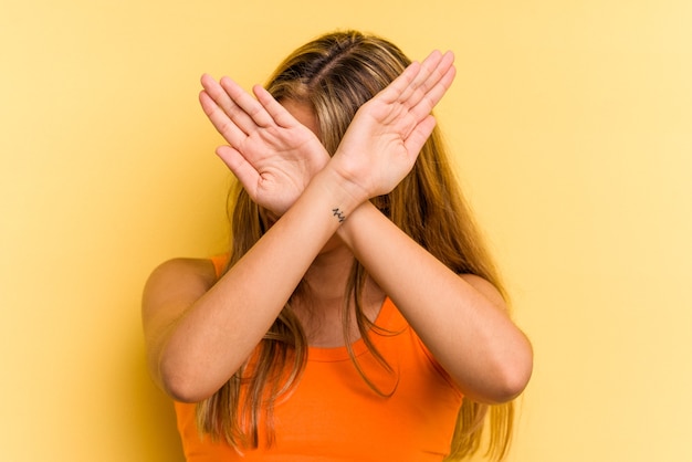 Jonge blanke blonde vrouw geïsoleerd op gele achtergrond houden twee armen gekruist, ontkenning concept.