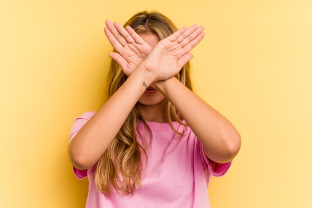 Jonge blanke blonde vrouw geïsoleerd op gele achtergrond houden twee armen gekruist, ontkenning concept.