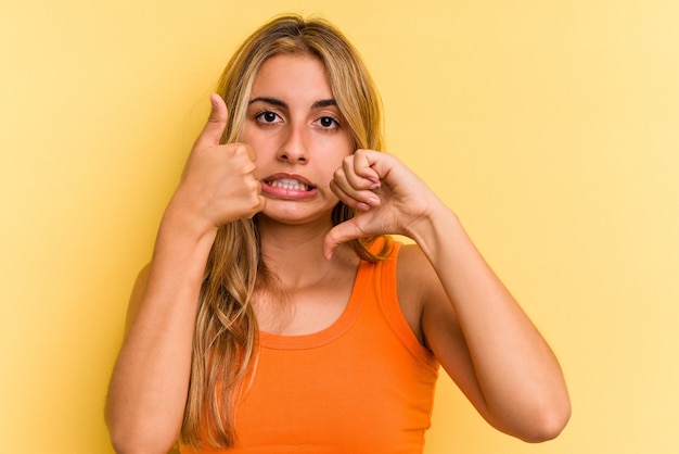 Jonge blanke blonde vrouw geïsoleerd op gele achtergrond met duimen omhoog en duim omlaag, moeilijk kies concept