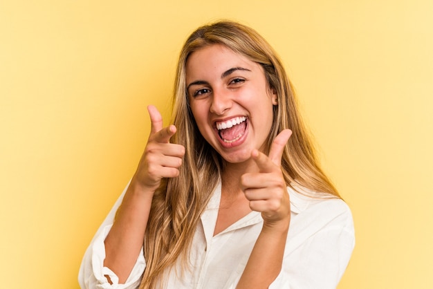 Jonge blanke blonde vrouw geïsoleerd op gele achtergrond wijzend naar voren met vingers.