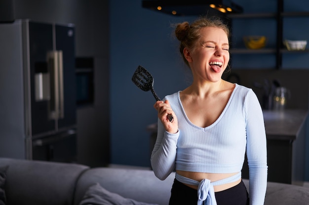 Foto jonge blanke blonde vrouw met een zwarte spatel steekt tong uit met haar ogen dicht lachend