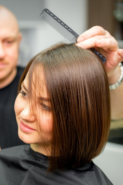 Jonge blanke brunette vrouw met haar hairstyling door een mannelijke kapper in een salon.