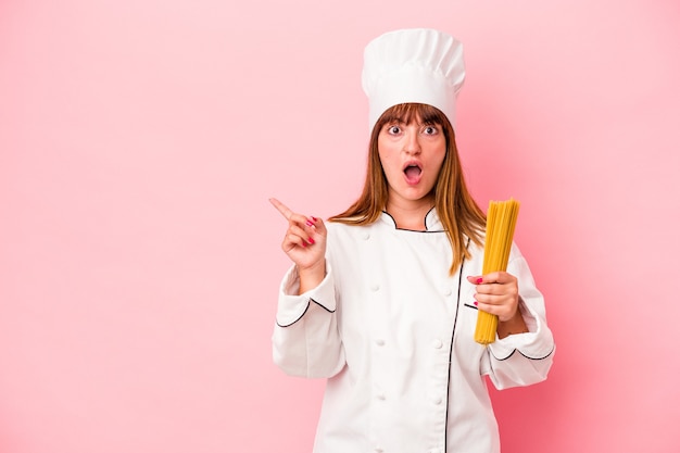 Jonge blanke chef-kokvrouw met pasta geïsoleerd op een roze achtergrond die naar de zijkant wijst