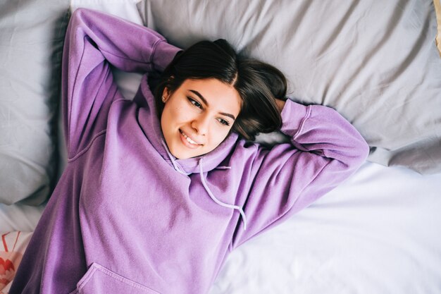 Jonge blanke dromerige vrouw glimlachend en liggend op een bed.