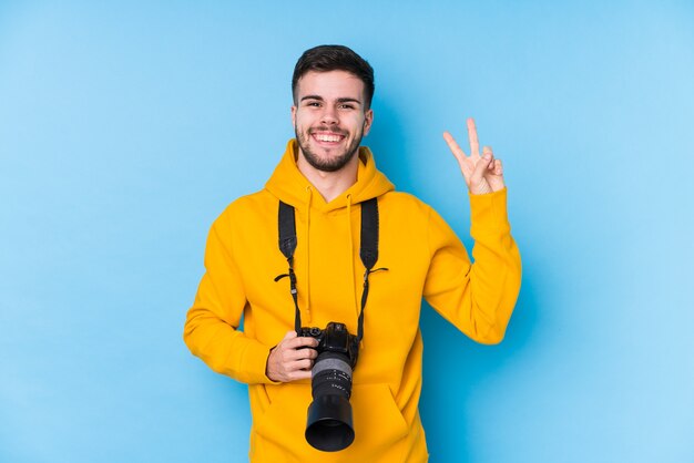 Jonge blanke fotograaf man geïsoleerd blij en zorgeloos met een vredessymbool met vingers.