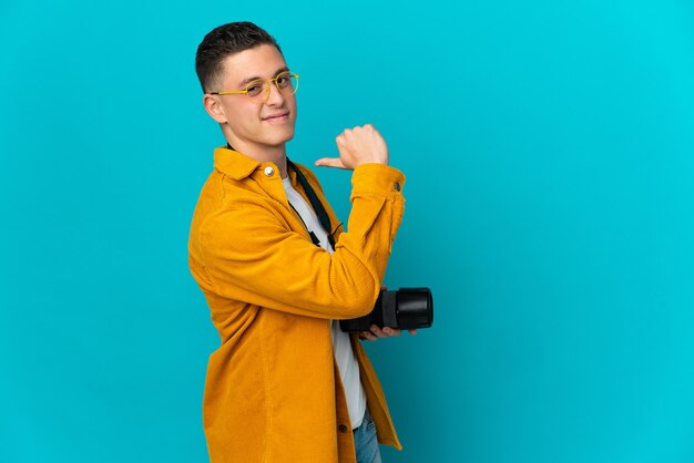 Jonge blanke fotograaf man geïsoleerd op blauwe muur trots en zelfvoldaan