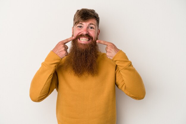 Jonge blanke gember man met lange baard geïsoleerd op een witte achtergrond glimlacht, wijzende vingers naar de mond.