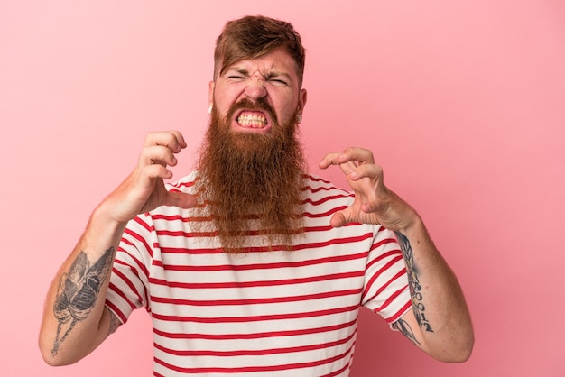 Jonge blanke gember man met lange baard geïsoleerd op roze achtergrond boos schreeuwen met gespannen handen.