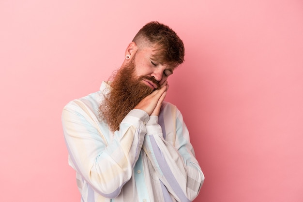 Jonge blanke gember man met lange baard geïsoleerd op roze achtergrond geeuwen met een vermoeid gebaar dat de mond bedekt met de hand.