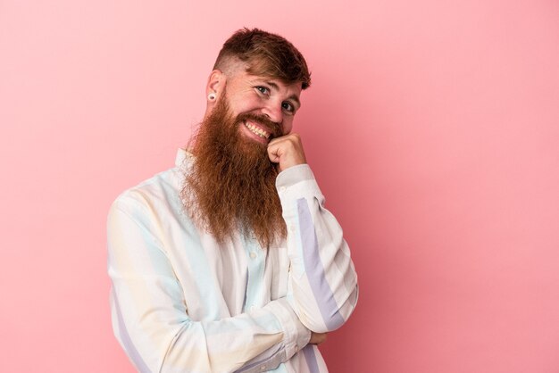 Jonge blanke gember man met lange baard geïsoleerd op roze achtergrond glimlachend gelukkig en zelfverzekerd, kin met de hand aanraken.