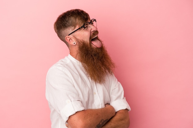 Jonge blanke gember man met lange baard geïsoleerd op roze achtergrond grappig en vriendelijk tong uitsteekt.