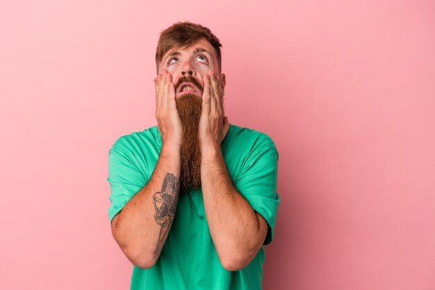 Jonge blanke gember man met lange baard geïsoleerd op roze achtergrond jammerend en huilend troosteloos.