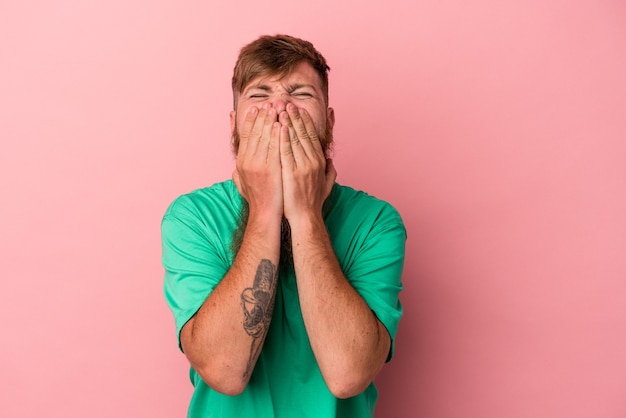 Jonge blanke gember man met lange baard geïsoleerd op roze achtergrond lachen om iets, mond bedekken met handen.