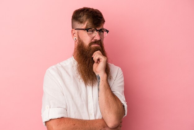 Jonge blanke gember man met lange baard geïsoleerd op roze achtergrond lijdt aan pijn in de keel als gevolg van een virus of infectie.