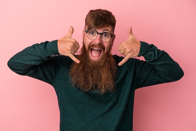 Jonge blanke gember man met lange baard geïsoleerd op roze achtergrond met een mobiel telefoongesprek gebaar met vingers.