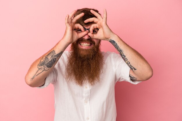 Foto jonge blanke gember man met lange baard geïsoleerd op roze achtergrond opgewonden houden ok gebaar in de gaten.