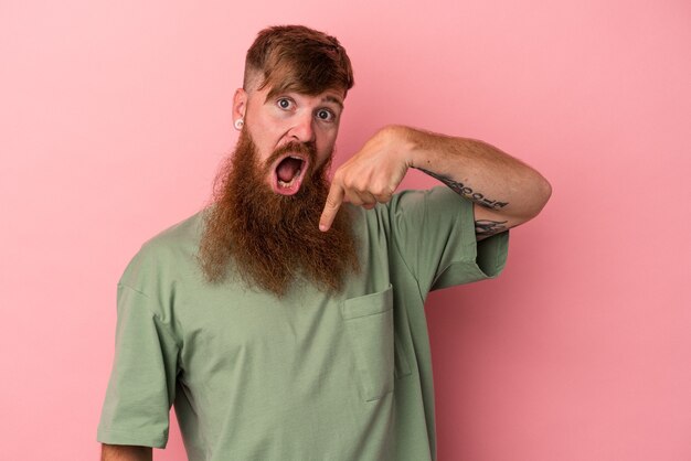 Jonge blanke gember man met lange baard geïsoleerd op roze achtergrond persoon met de hand wijzend naar een shirt kopie ruimte, trots en zelfverzekerd