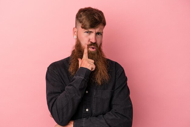 Jonge blanke gember man met lange baard geïsoleerd op roze achtergrond zijwaarts kijkend met twijfelachtige en sceptische uitdrukking.