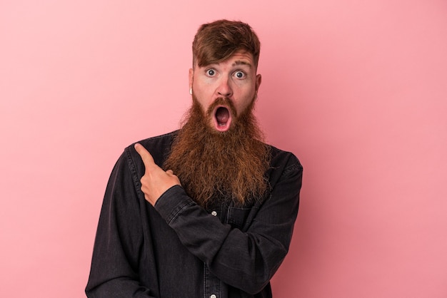 Jonge blanke gemberman met lange baard geïsoleerd op een roze achtergrond die naar de zijkant wijst