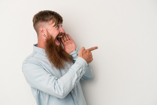 Jonge blanke gemberman met lange baard geïsoleerd op een witte achtergrond die een roddel zegt, wijzend naar de zijkant die iets meldt.