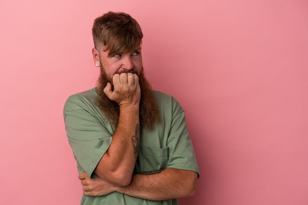 Jonge blanke gemberman met lange baard geïsoleerd op roze achtergrond bijtende vingernagels, nerveus en erg angstig.