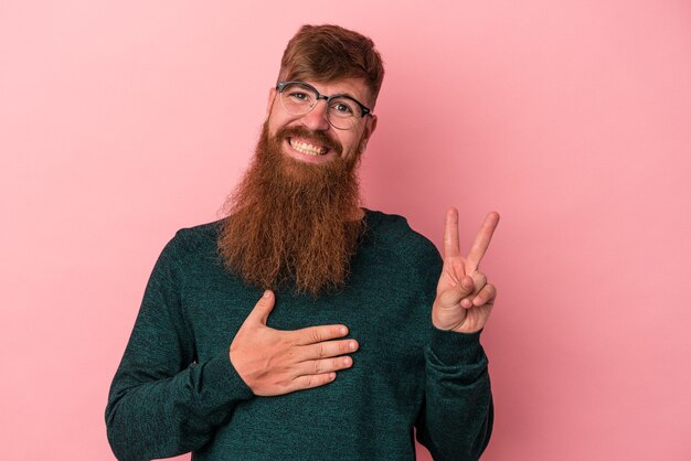 Jonge blanke gemberman met lange baard geïsoleerd op roze achtergrond die een eed aflegt, hand op de borst.