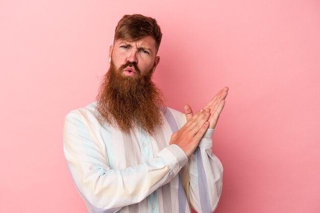 Jonge blanke gemberman met lange baard geïsoleerd op roze achtergrond voelt zich energiek en comfortabel en wrijft zelfverzekerd over de handen.