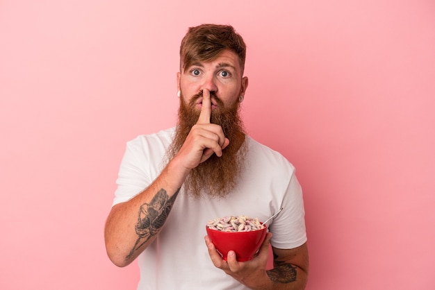 Jonge blanke gemberman met lange baard met een kom cornflakes geïsoleerd op roze achtergrond die een geheim houdt of om stilte vraagt.