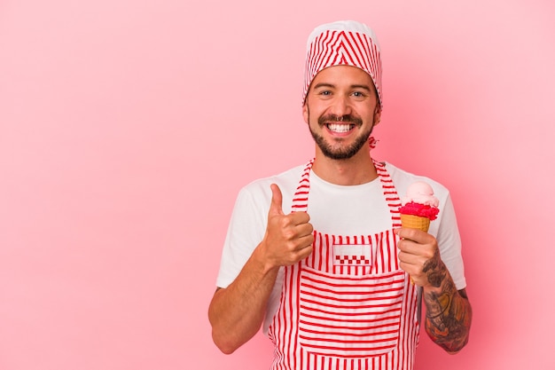 Jonge blanke ijsmaker man met tatoeages met ijs geïsoleerd op roze achtergrond glimlachend en duim omhoog