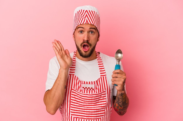 Jonge blanke ijsmaker man met tatoeages met lepel geïsoleerd op roze achtergrond verrast en geschokt.