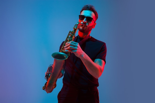 Jonge blanke jazzmuzikant die saxofoon speelt in neonlicht
