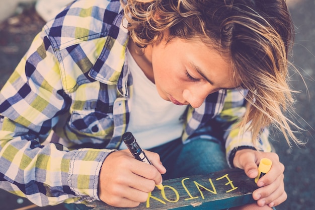 Jonge blanke jongen man schrijft een bord met geniet van een bericht op een houten stuk