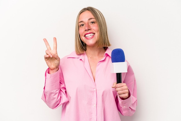 Jonge blanke journaliste vrouw geïsoleerd op een witte achtergrond blij en zorgeloos met een vredessymbool met vingers