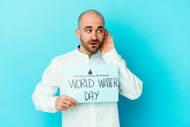 Jonge blanke kale man vieren wereld water dag geïsoleerd op blauw proberen te luisteren een roddels.