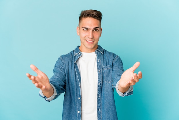 Jonge blanke knappe man geïsoleerd maakt schaal met armen, voelt zich gelukkig en zelfverzekerd.