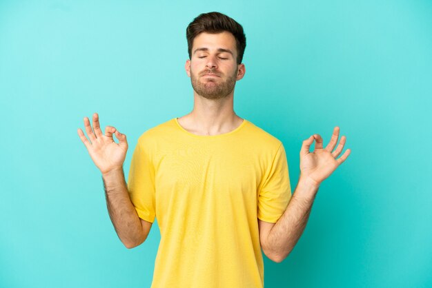 Jonge blanke knappe man geïsoleerd op blauwe achtergrond in zen pose