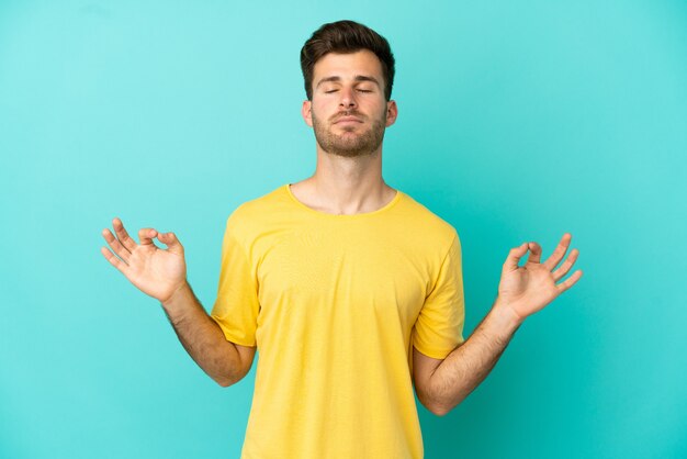 Jonge blanke knappe man geïsoleerd op blauwe achtergrond in zen pose