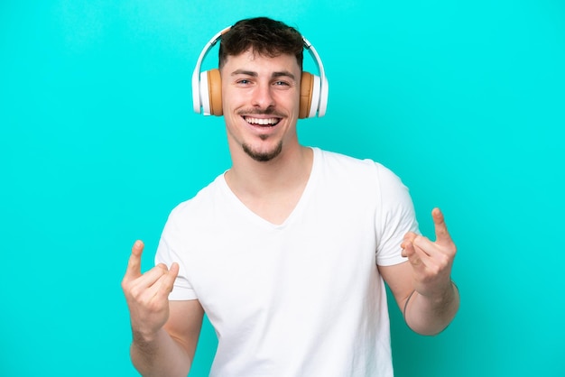 Jonge blanke knappe man geïsoleerd op blauwe achtergrond luisteren muziek maken rock gebaar