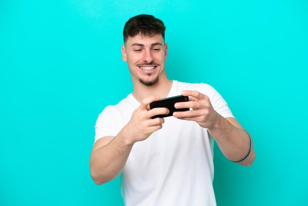 Jonge blanke knappe man geïsoleerd op blauwe achtergrond spelen met de mobiele telefoon