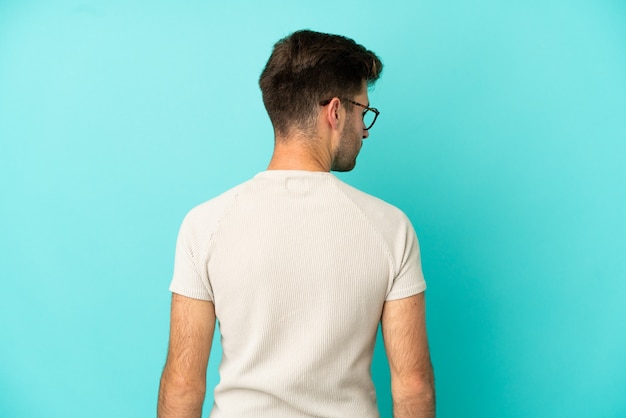 Jonge blanke knappe man geïsoleerd op een blauwe achtergrond in de achterste positie en op zoek naar de zijkant