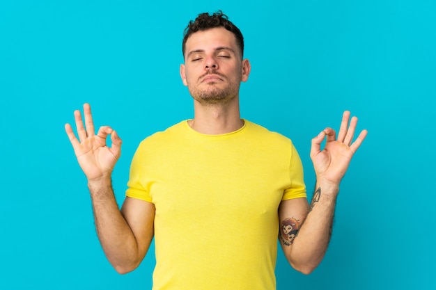 Jonge blanke knappe man geïsoleerd op een blauwe achtergrond in zen pose