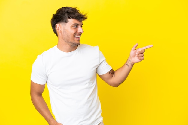 Jonge blanke knappe man geïsoleerd op een gele achtergrond die met de vinger naar de zijkant wijst en een product presenteert