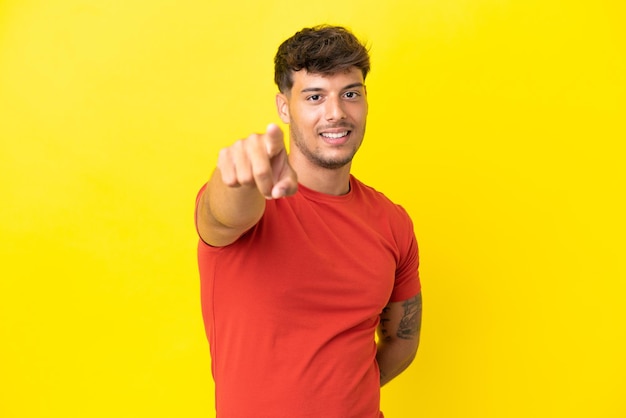 Jonge blanke knappe man geïsoleerd op een gele achtergrond die naar voren wijst met een gelukkige uitdrukking