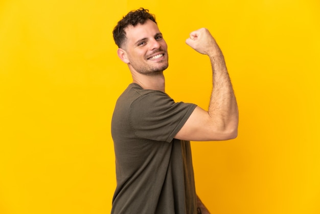 Jonge blanke knappe man geïsoleerd op geel doet sterk gebaar