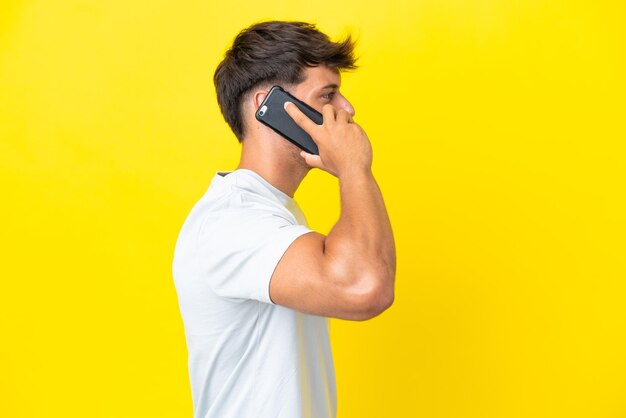 Jonge blanke knappe man geïsoleerd op gele achtergrond een gesprek met de mobiele telefoon met iemand houden
