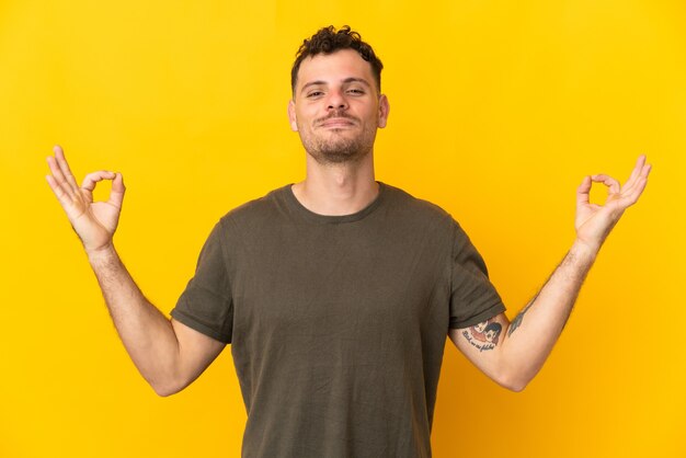 Jonge blanke knappe man geïsoleerd op gele muur in zen pose