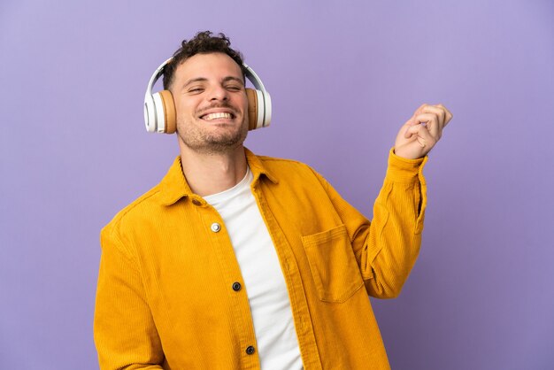 Jonge blanke knappe man geïsoleerd op paarse muur luisteren muziek en gitaar gebaar doen